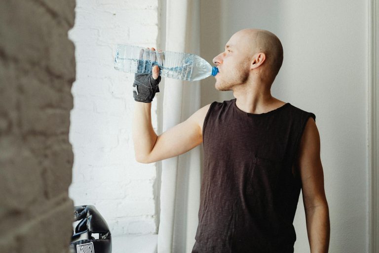 Bald man drinking bottled water indoors, embracing a healthy lifestyle.